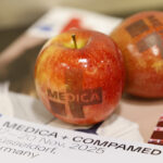 Manzanas con el logotipo de MEDICA sobre material promocional de MEDICA y COMPAMED en Düsseldorf.