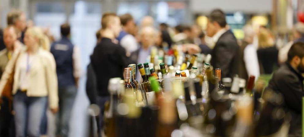 Botellas de vino expuestas en un stand ferial con visitantes profesionales al fondo